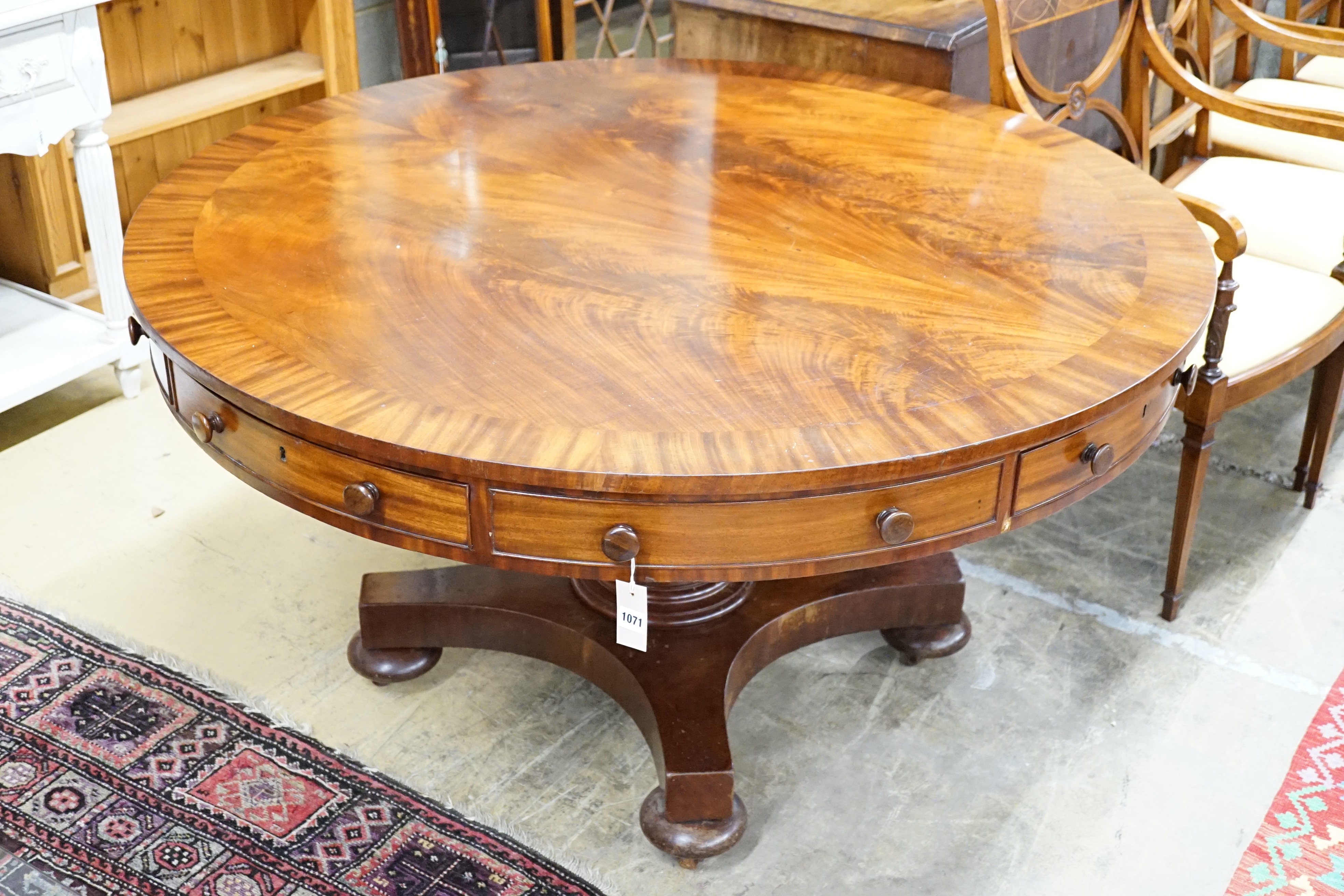 An early Victorian flame mahogany drum top ‘rent’ table, fitted four drawers on turned column saltire platform and brass castors, diameter 138cm, height 74cm